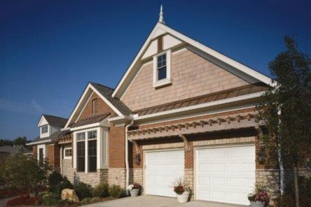 Before photo showing a Casa Grande home with two plain white garage doors and potted plants on the driveway.