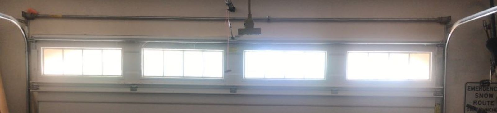 Interior view of a Coolidge garage showing a white sectional garage door with new cables installed and sunlight streaming through the upper windows.